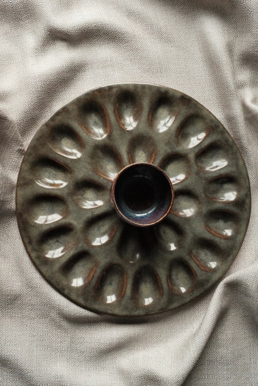 An overhead view of a dark olive-green deviled-egg platter with a ring of egg wells around a center dip well