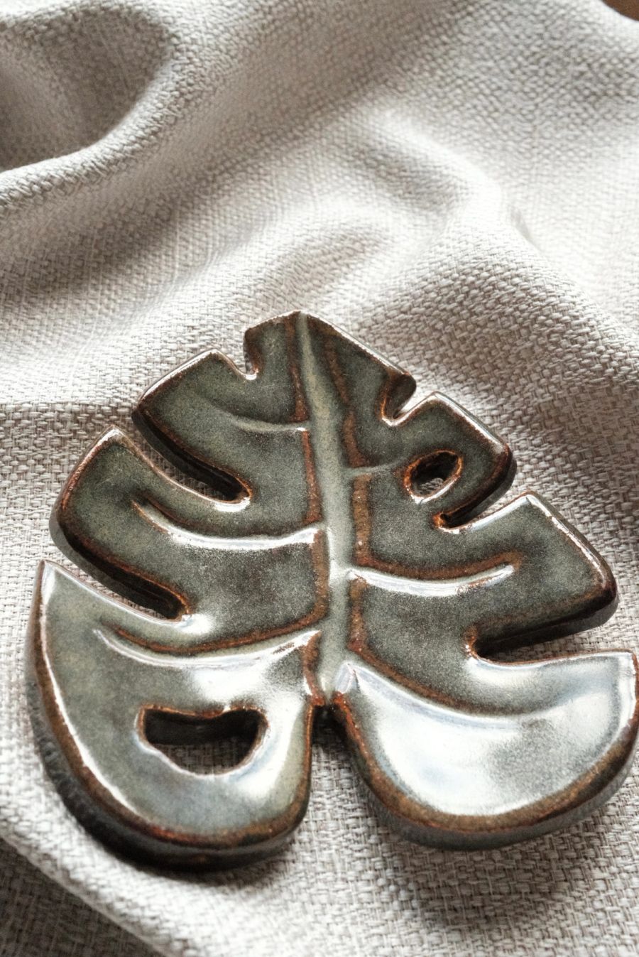 A close view of a sage-glazed monstera-leaf dish with hand-carved veining on white linen