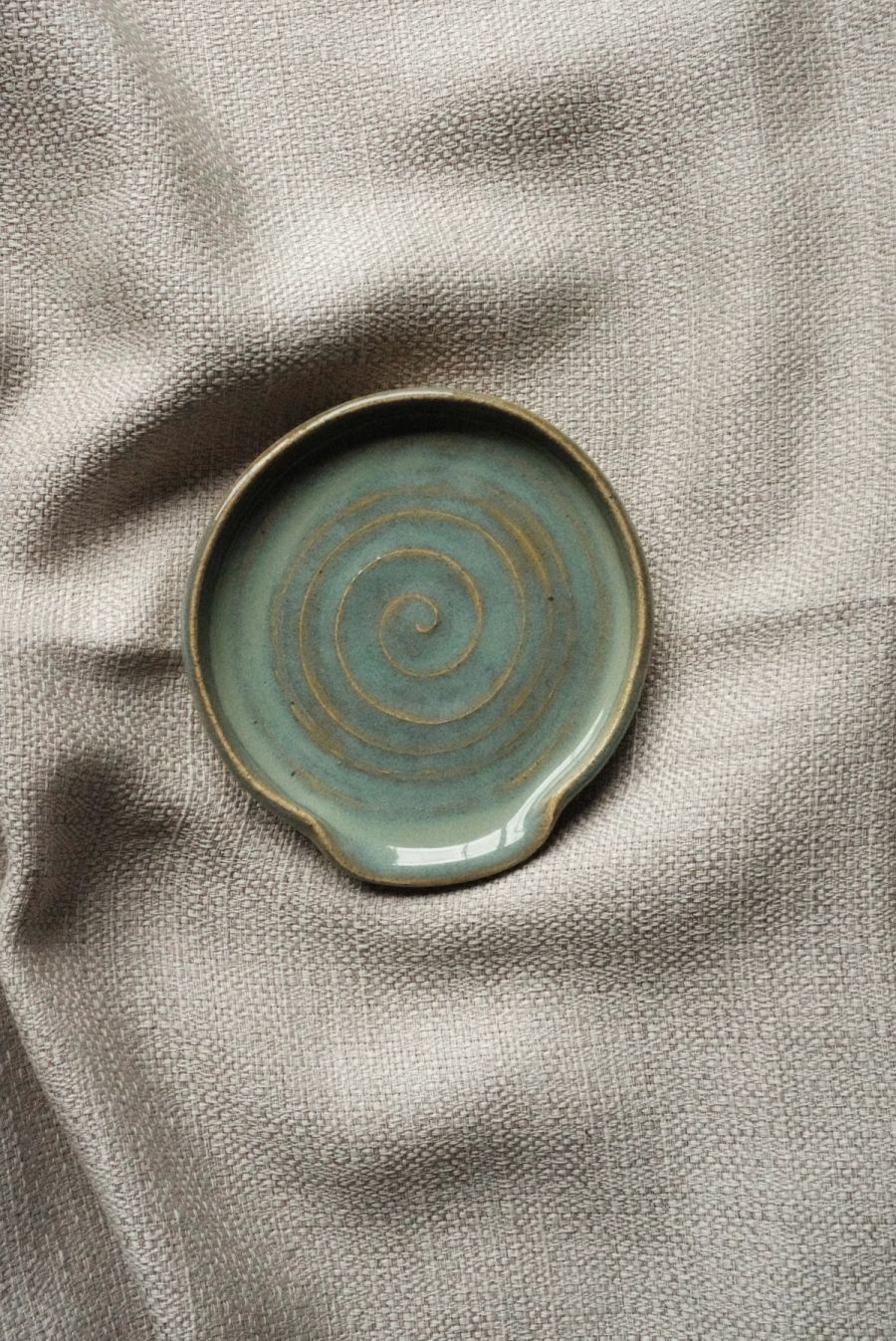 A round celadon spoon rest with a hand-thrown spiral, on linen