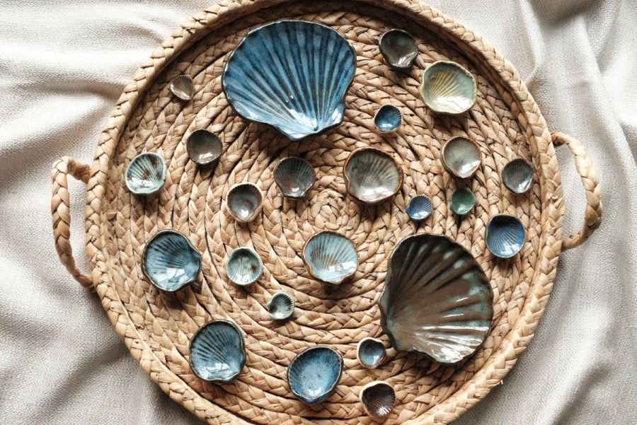 A blue scallop-shell dish surrounded by small round pebble dishes on a woven round placemat, seen from above