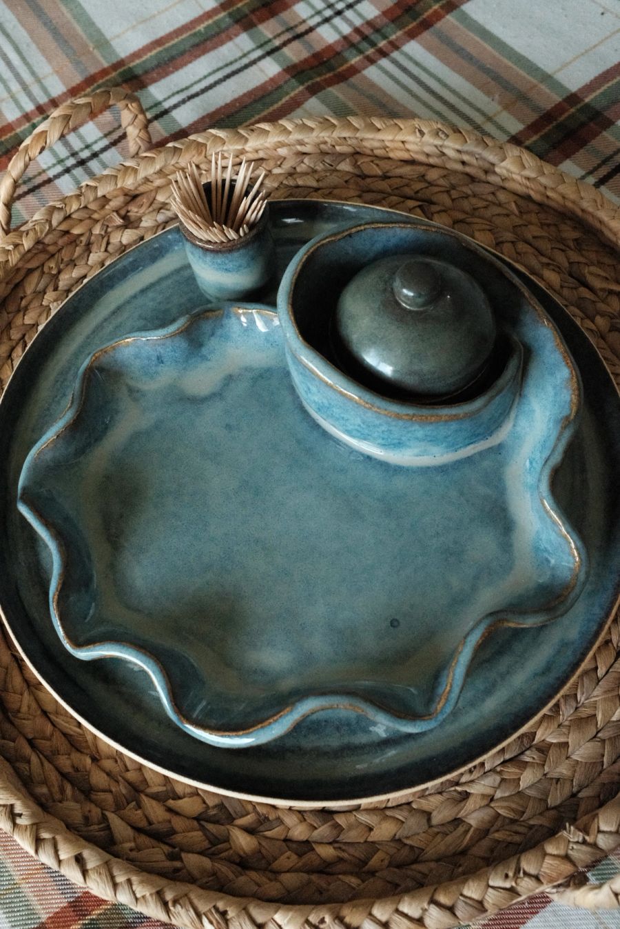 A blue-glazed ruffle-edged dish with a small lidded pot on a round woven tray
