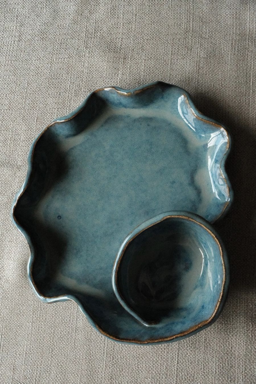 A blue ruffle-edged plate beside a small blue dip bowl on grey linen, seen from above