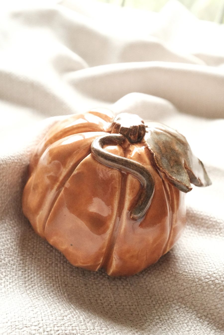 A terracotta-glazed lidded dish shaped like a pumpkin with a curling stem, on linen