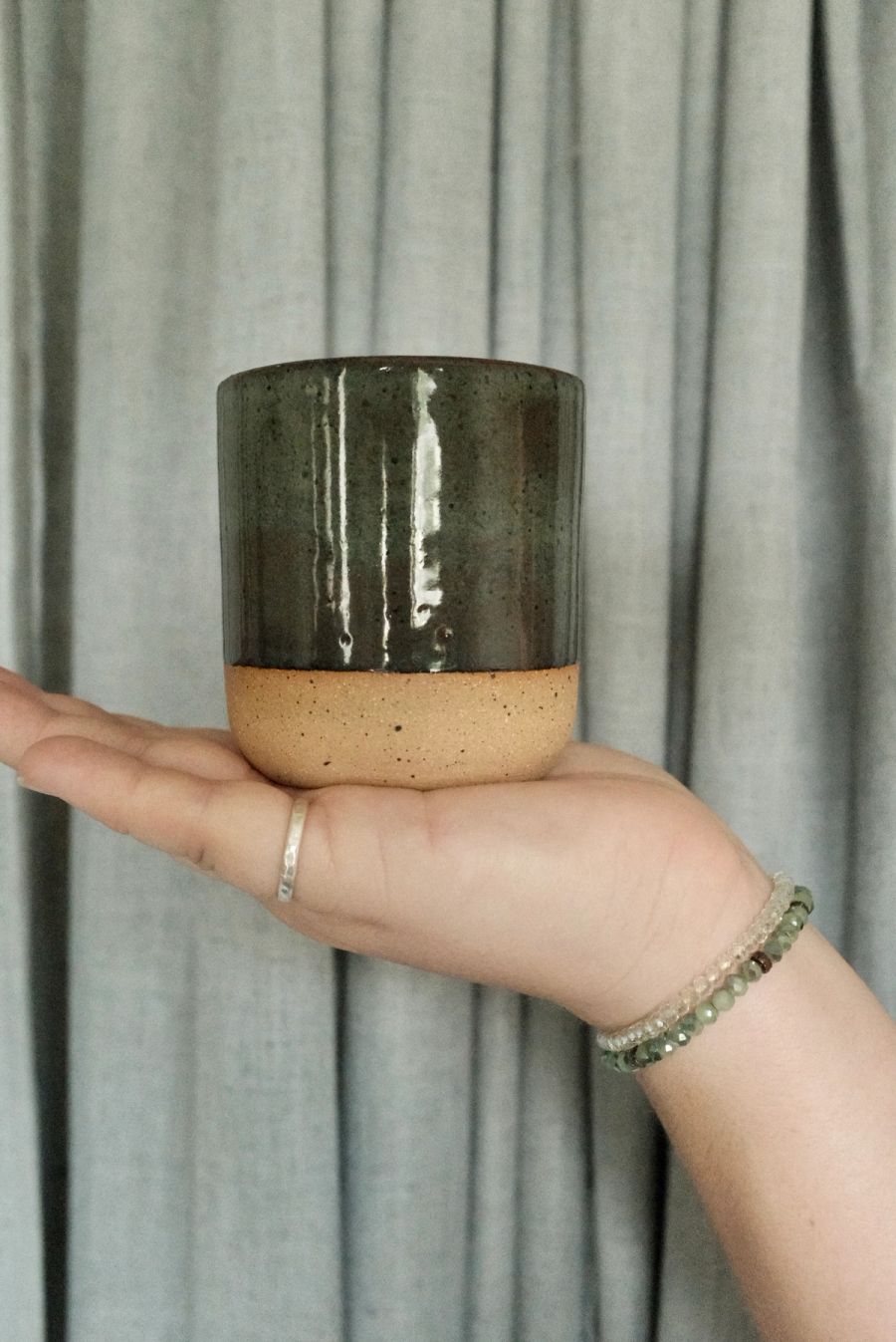 A hand holding an olive-green tumbler glazed over a raw clay base