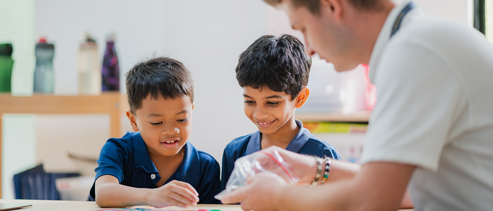 Invictus teacher assisting young primary students with a learning activity.