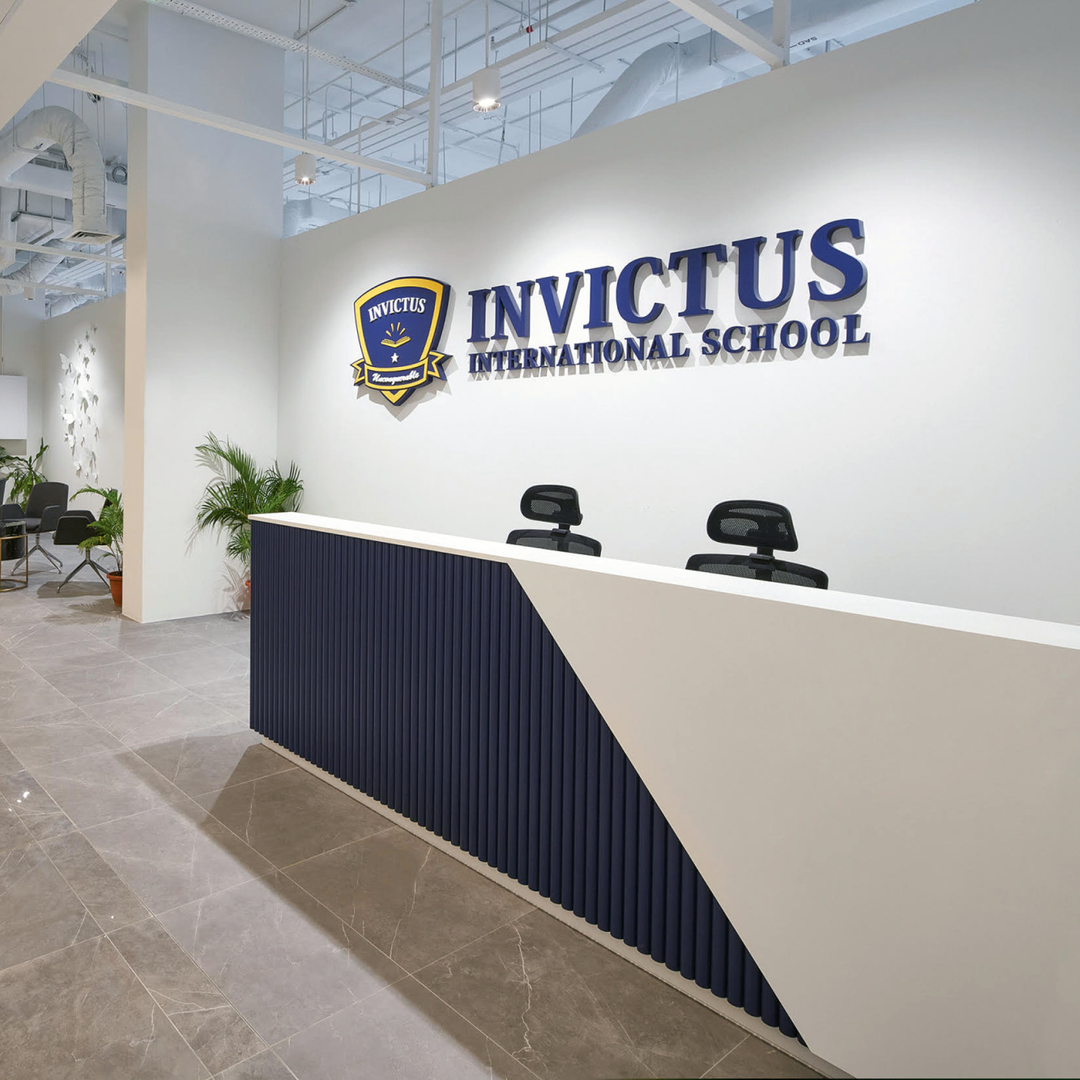 Reception area of Invictus International School's Centrium Square Campus in Singapore, featuring a modern front desk, school logo on the wall, indoor plants, and a contemporary waiting lounge.