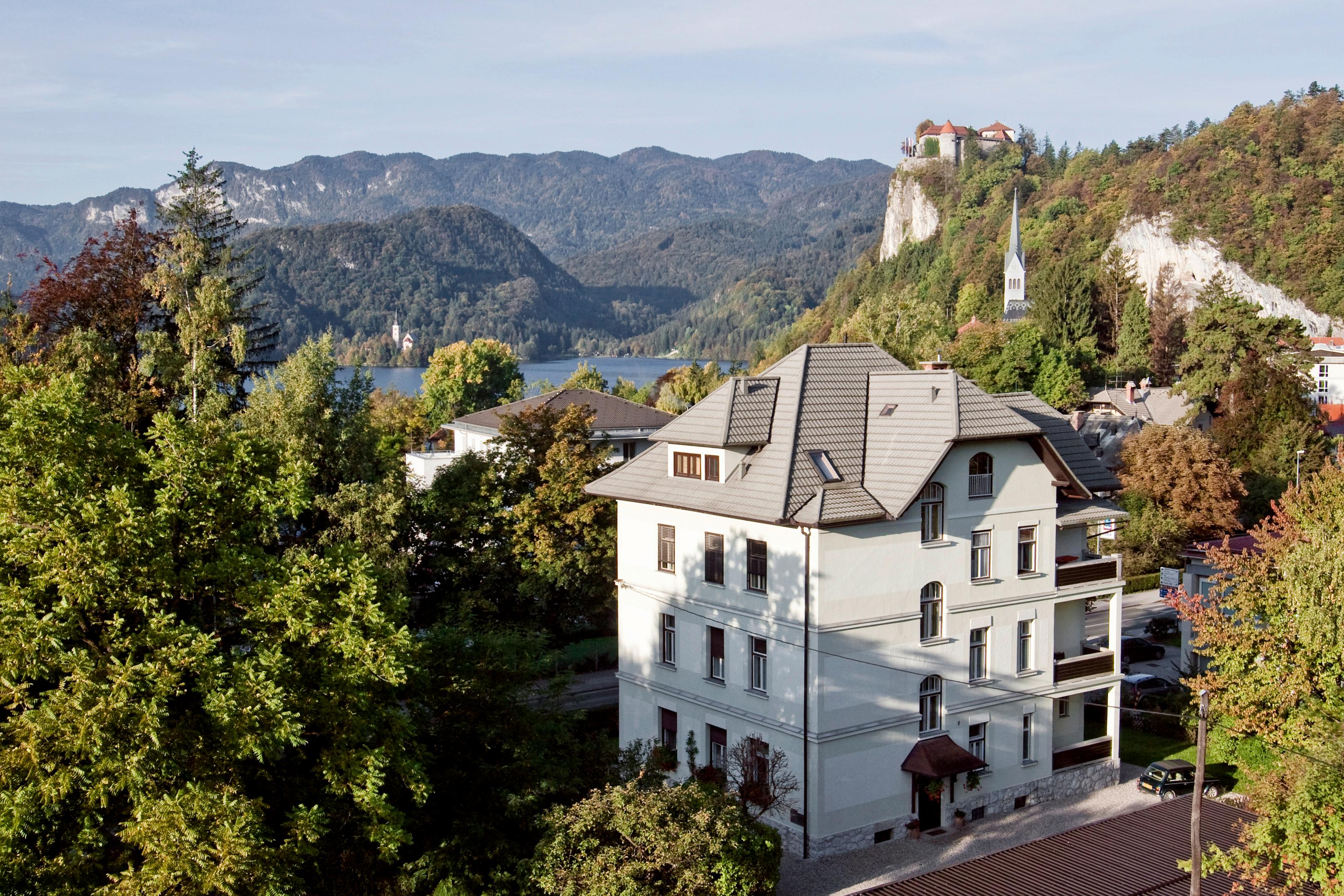 Panoramic view of the Josephine Village in Bled, with Lake Bled in the background and Bled Castle on top of the hill. The image highlights the architecture of the village in harmony with the mountainous landscape.