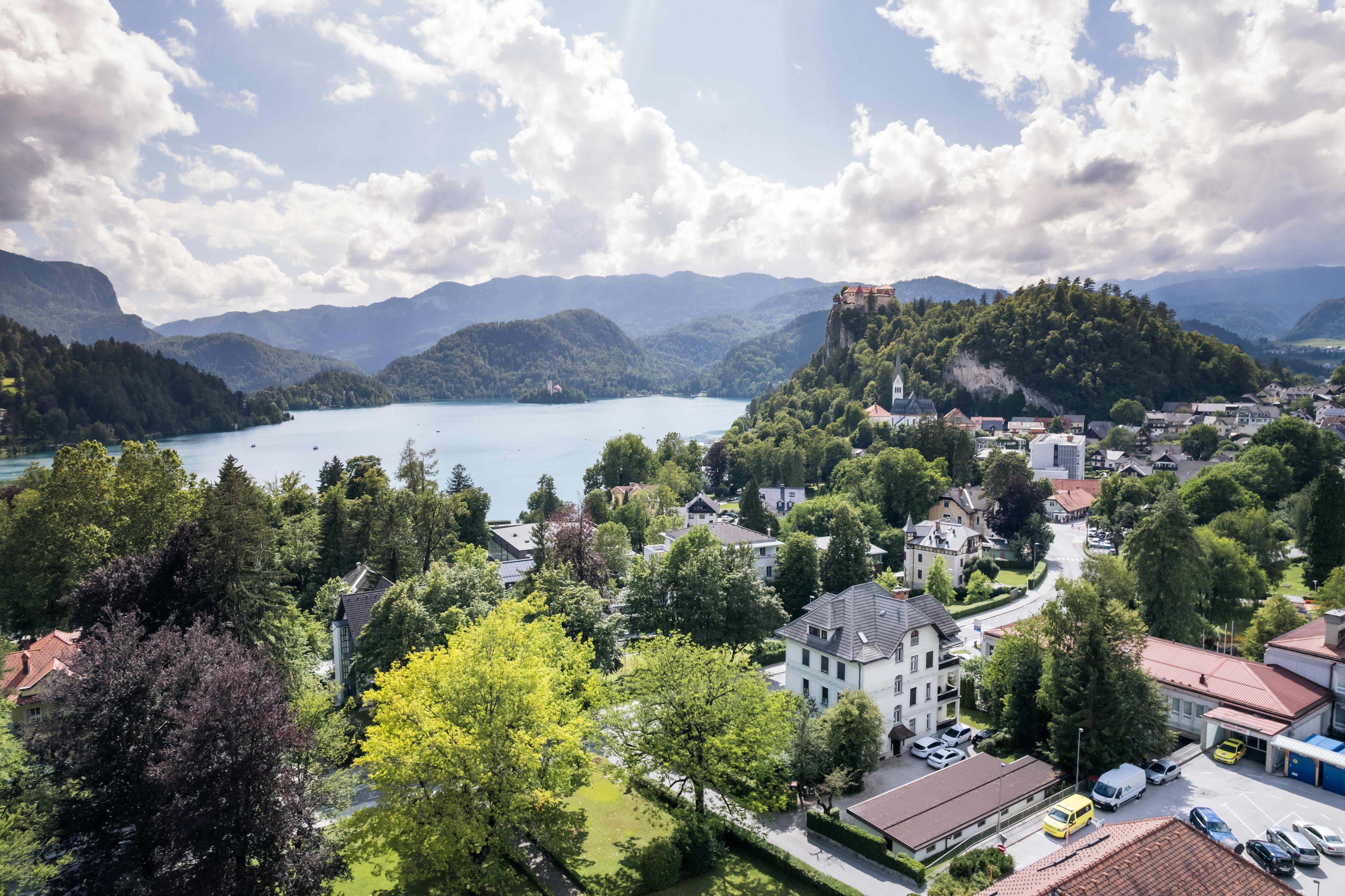 Aerial view of Lake Bled and the surrounding village, highlighting the Josephine Village, surrounded by trees and with the mountains in the background, creating a stunning landscape.