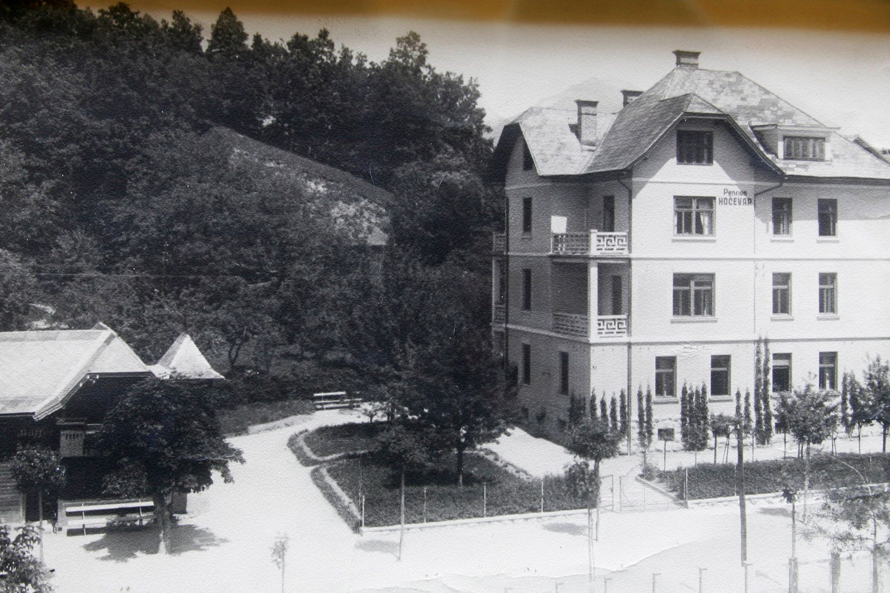 Historic image of Villa Josephine, showing the facade and well-kept garden, with benches along the path and the village in the background.