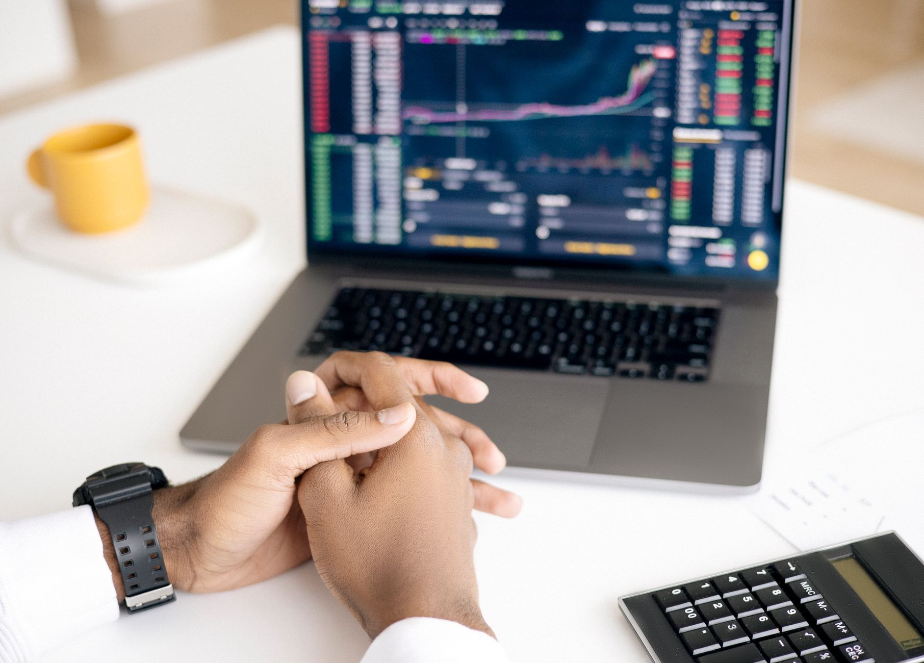 Hands resting beside a laptop showing live market data and a calculator