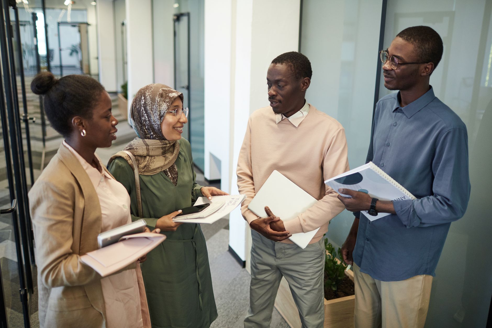 Four colleagues talking while holding documents in an office corridor