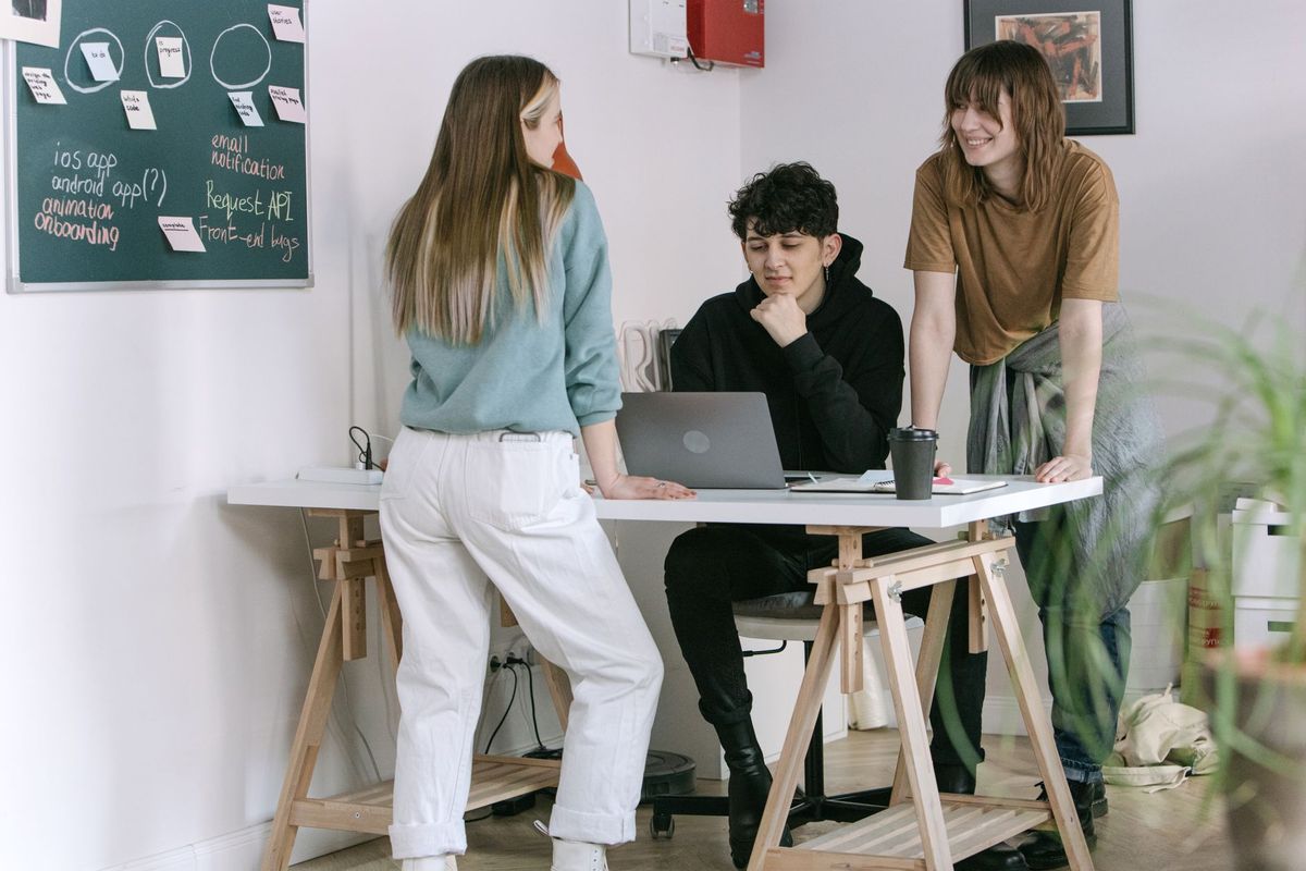 Three young coworkers around a standing desk in a bright studio