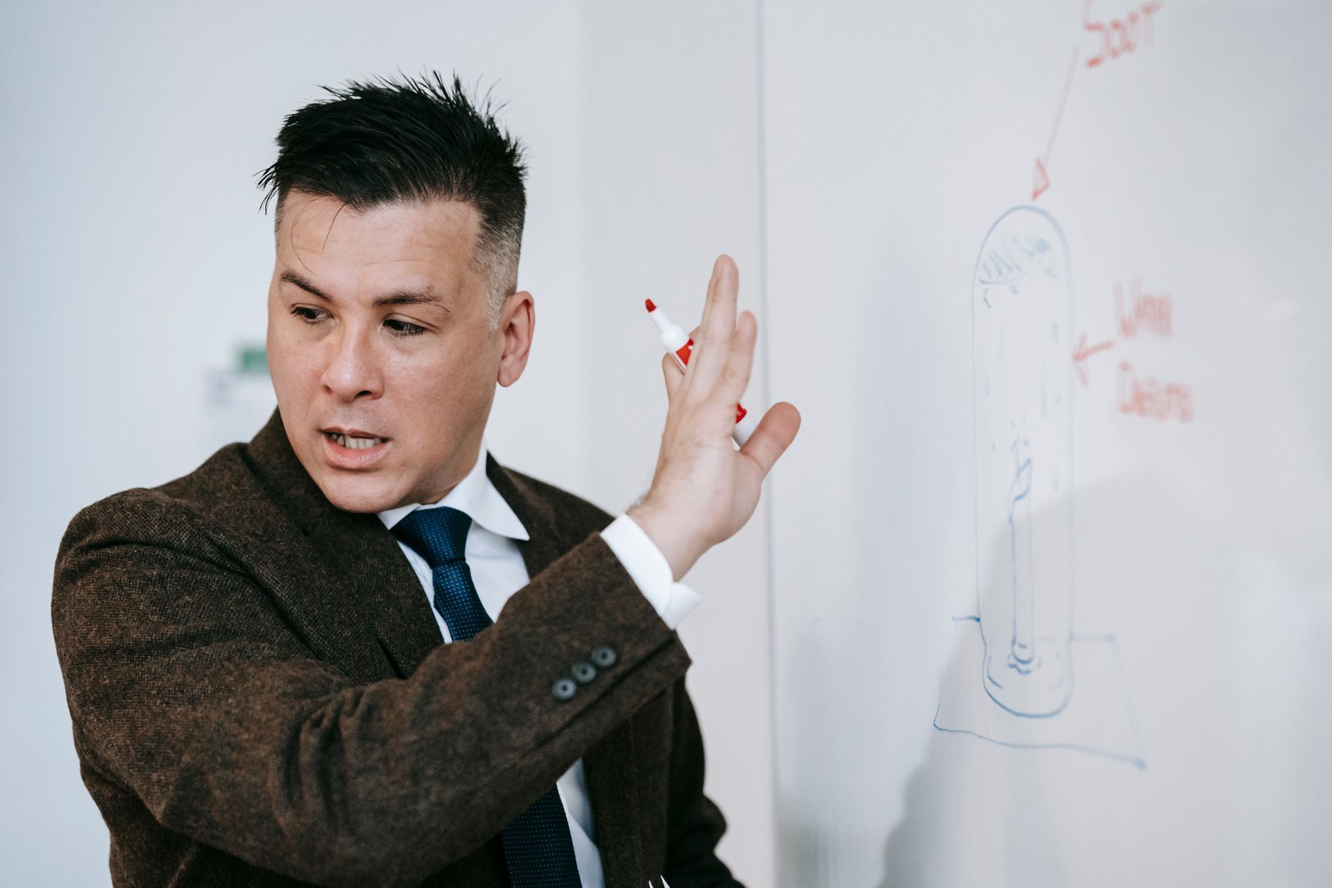 Man in a jacket explaining a diagram drawn on a glass whiteboard