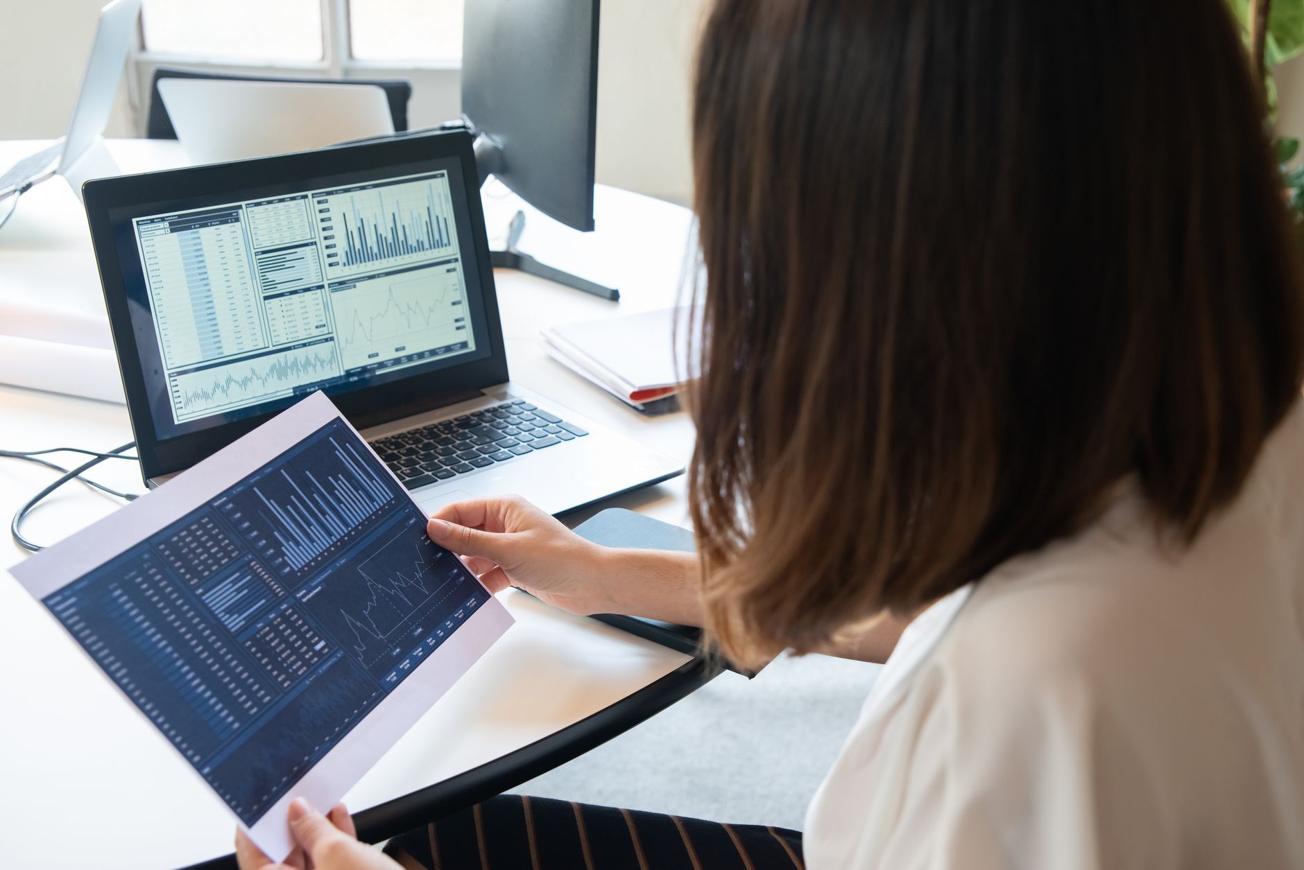 Woman reviewing market data across a laptop and tablet