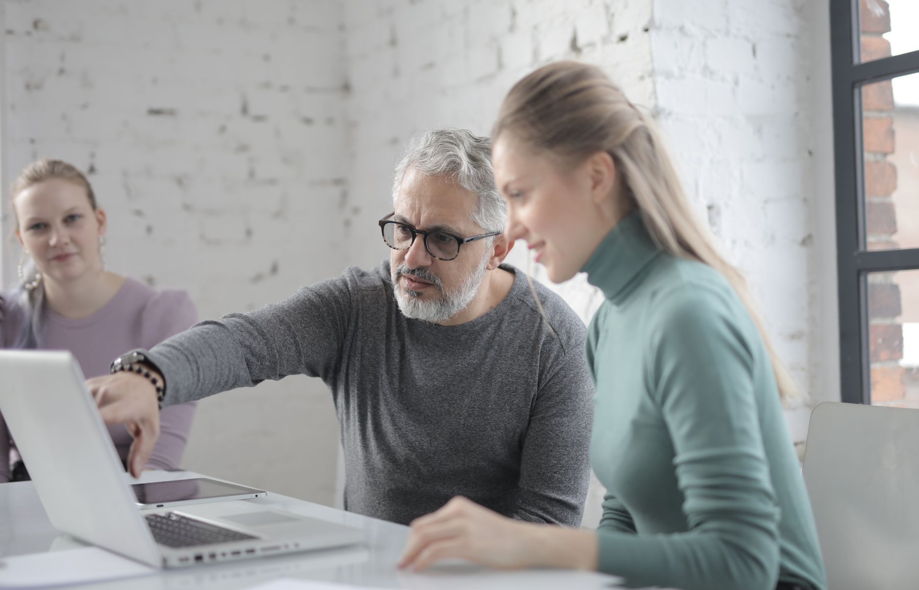 Experienced colleague explaining something on a laptop to two coworkers
