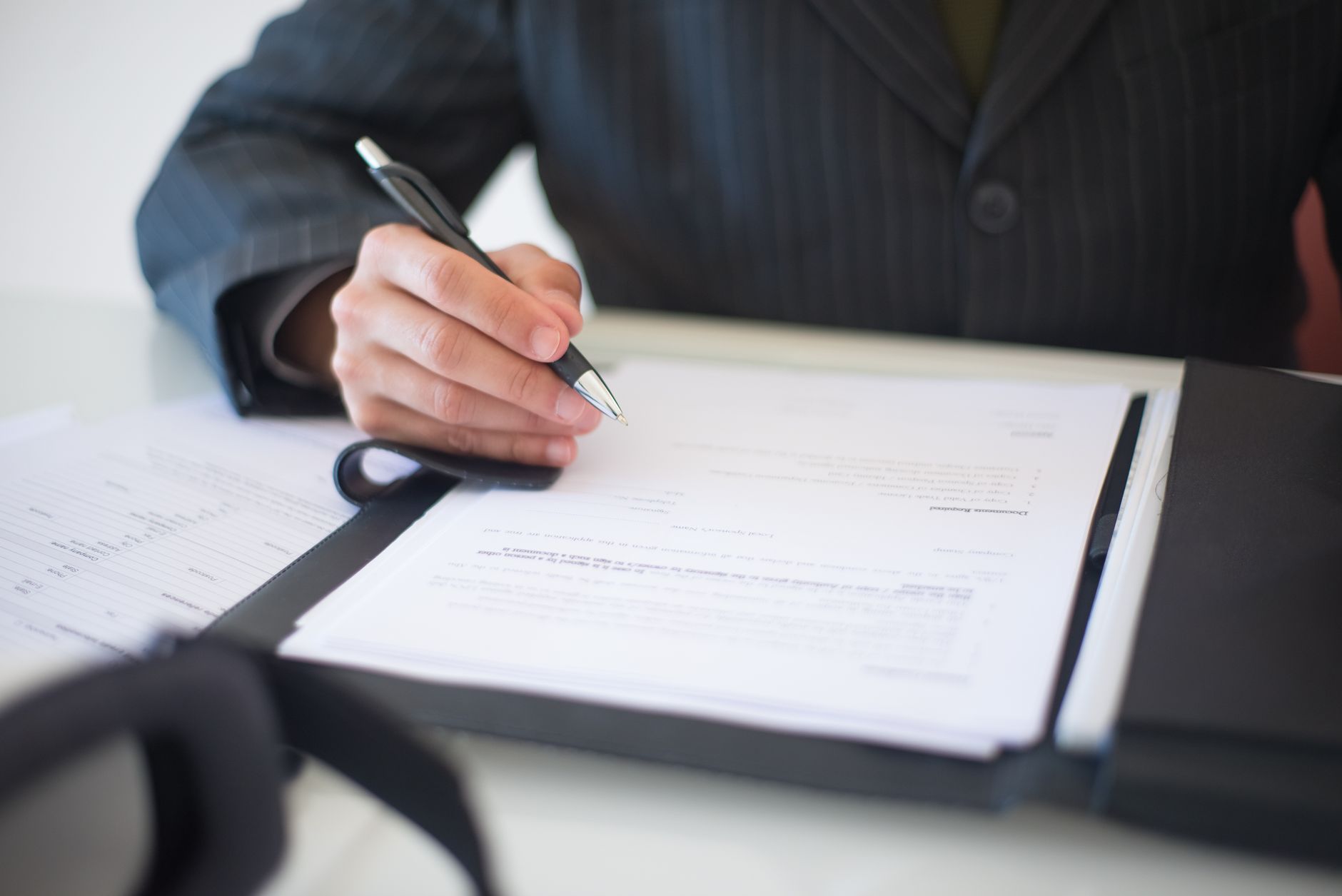 Person in a suit signing a document on a clipboard