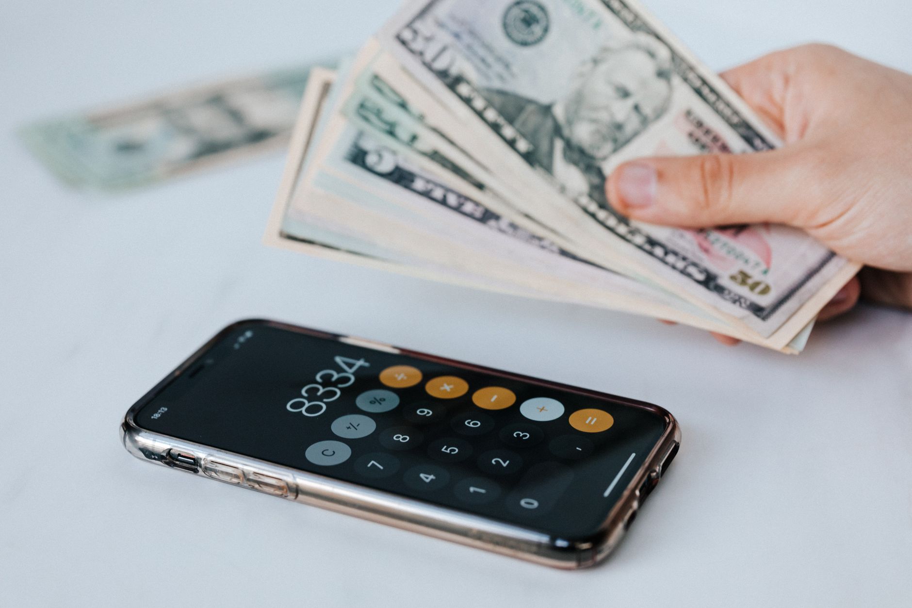 Hand holding a fan of cash above a phone showing a calculator