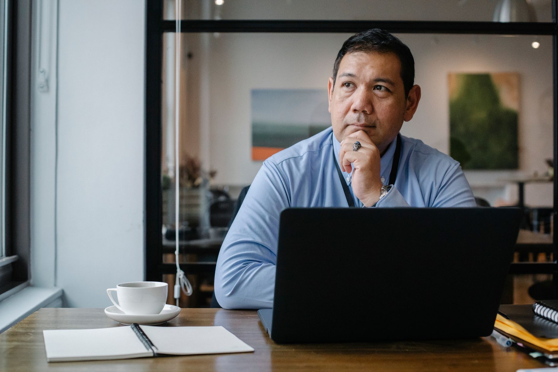 Man pausing in thought behind an open laptop in a home office