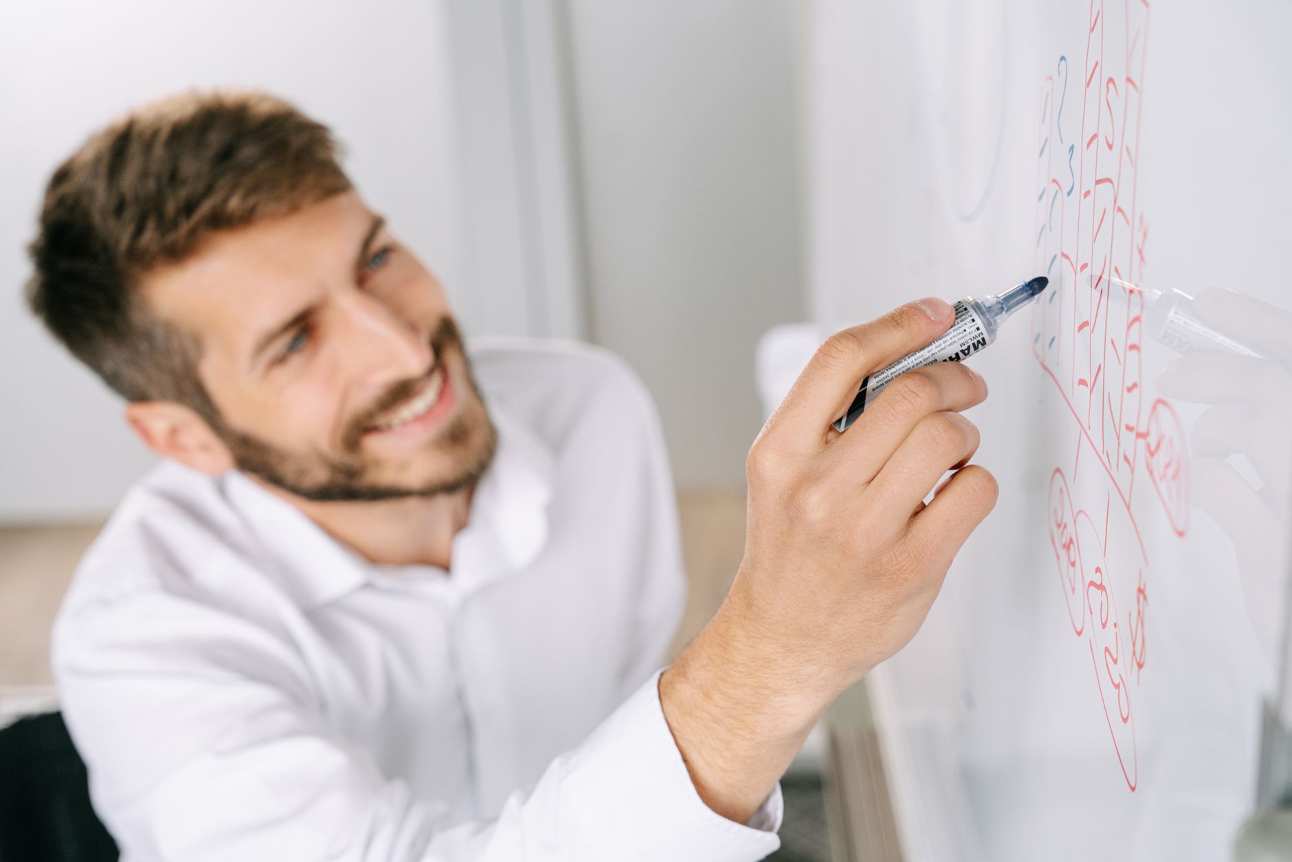 Man in a white shirt drawing a diagram on a glass whiteboard