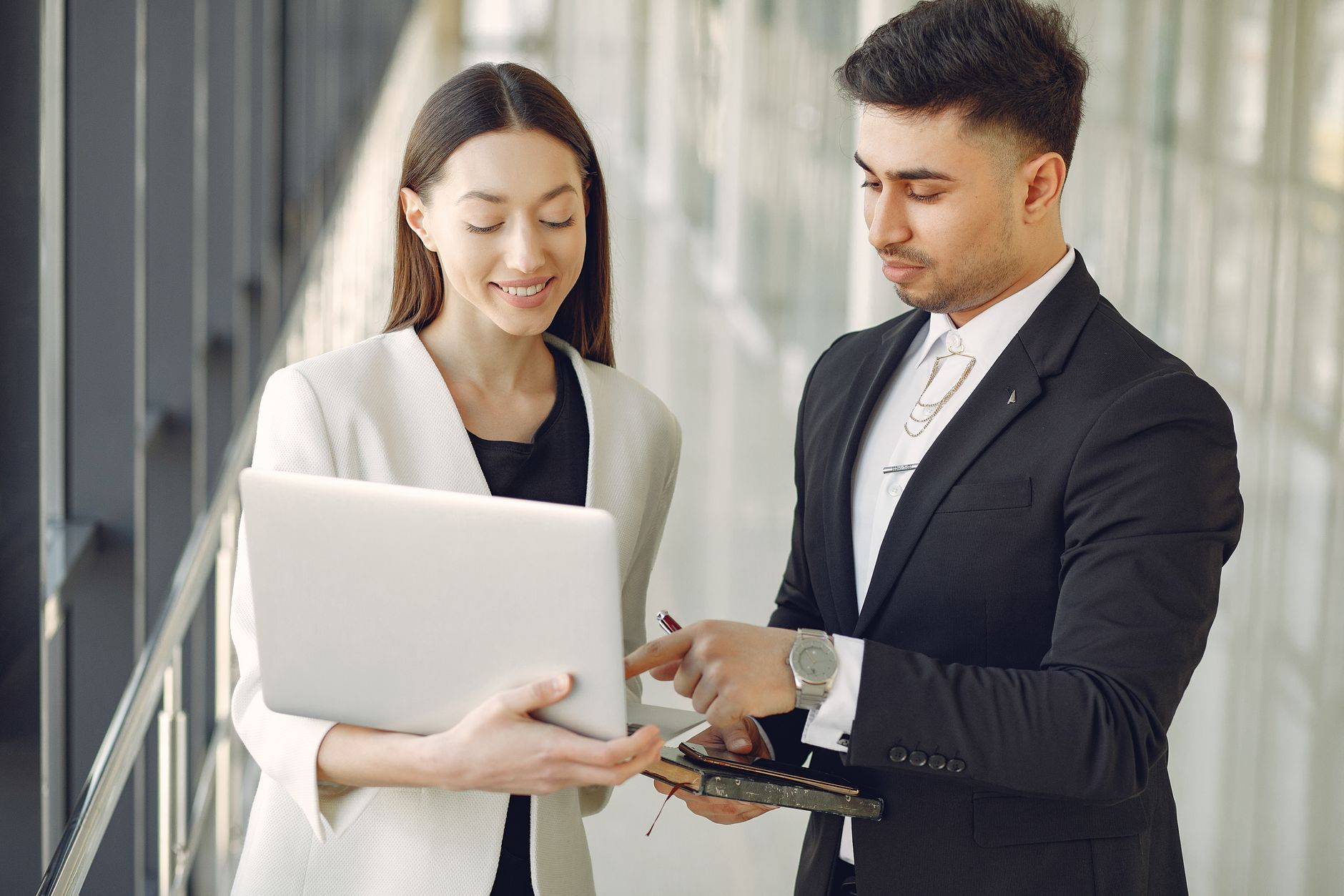 Two colleagues comparing notes on a laptop and a phone while standing