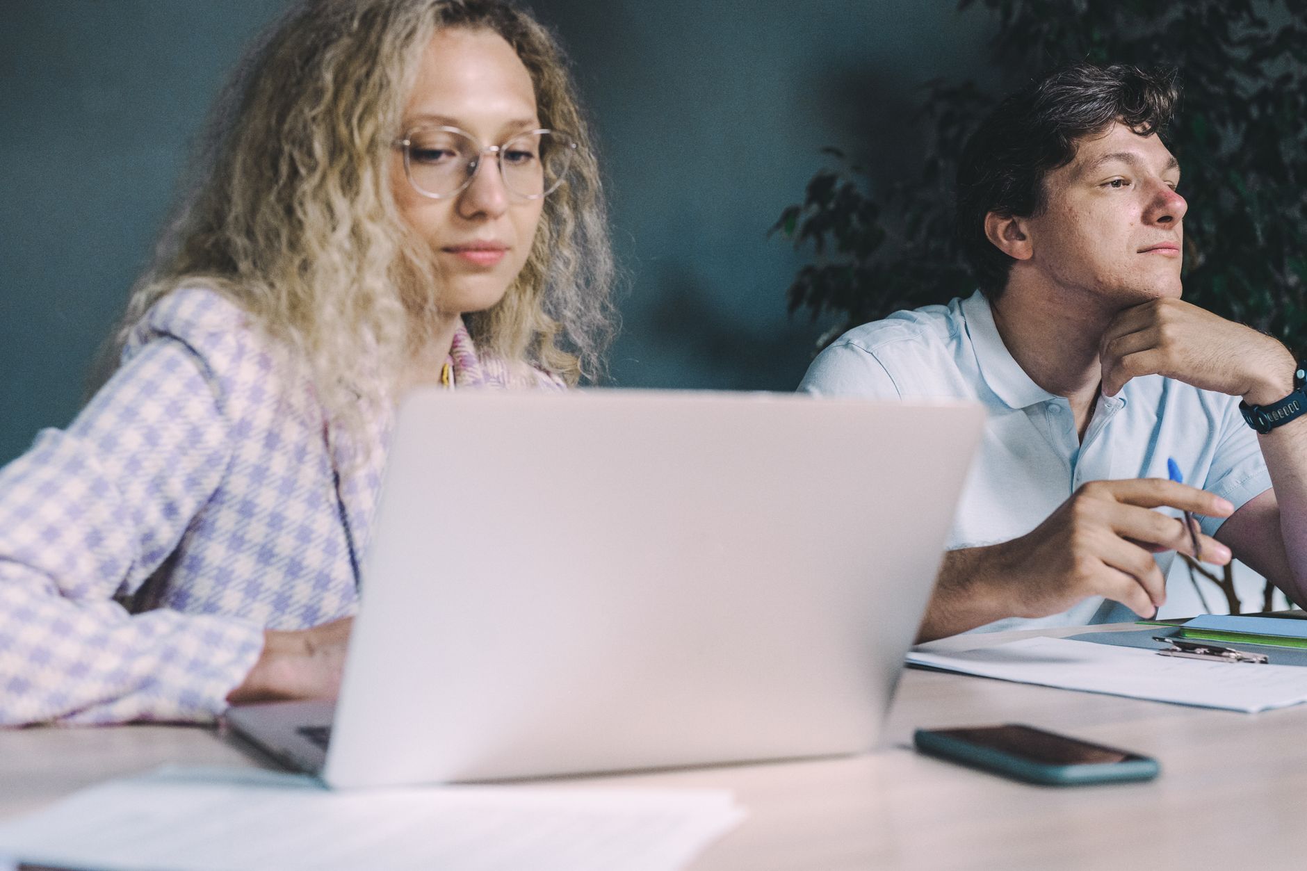 Two coworkers pausing to think in front of an open laptop