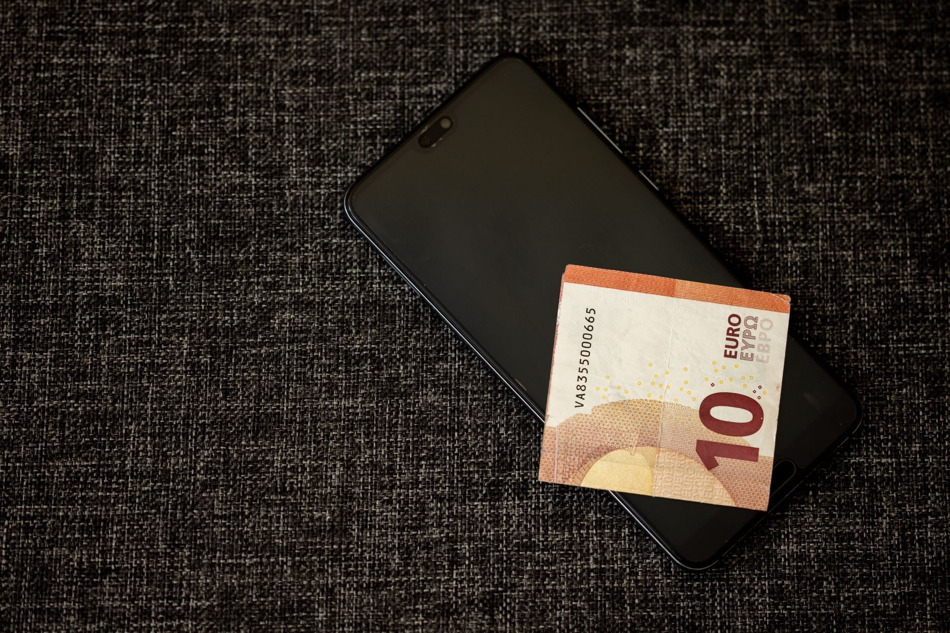 A ten euro note resting on a smartphone on a dark fabric surface