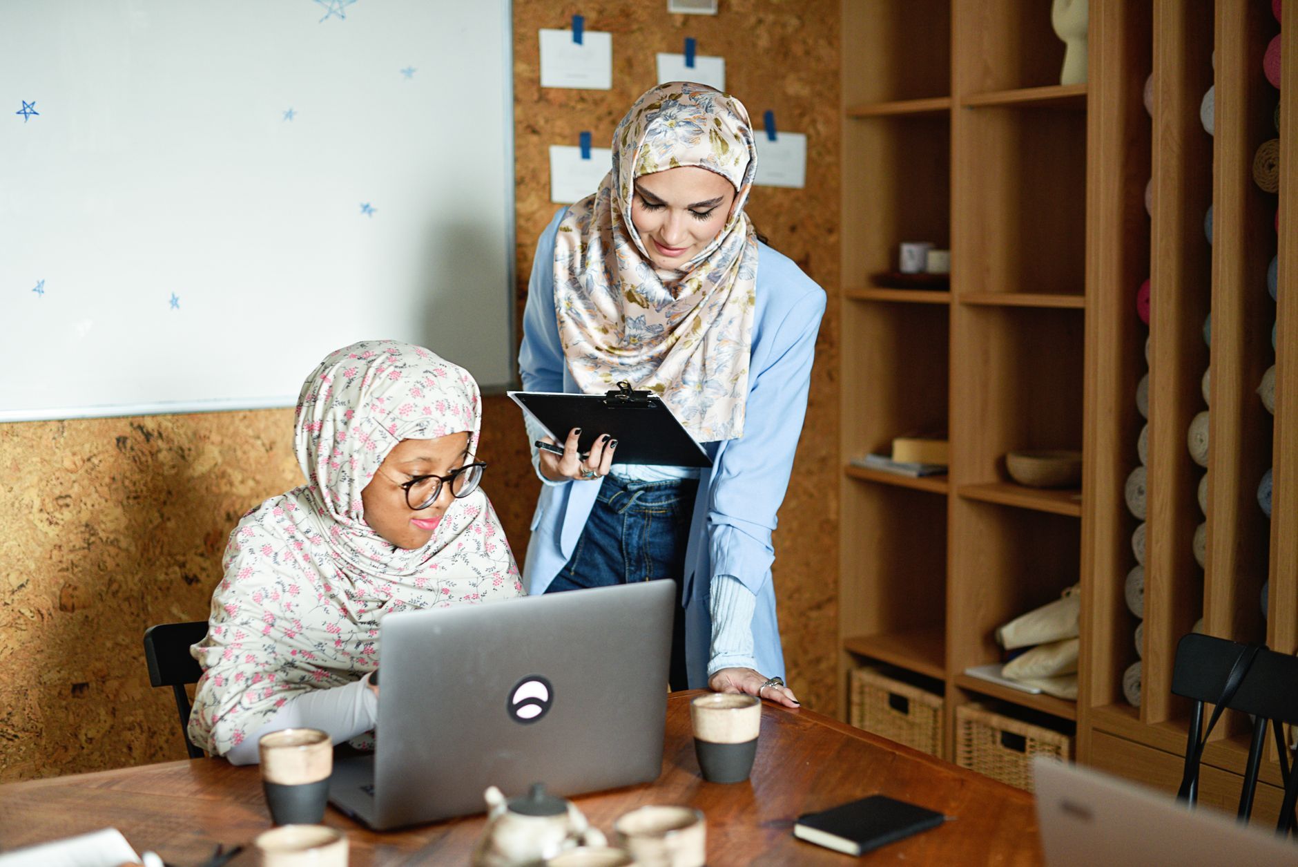 Two women working together on a laptop and tablet in a warm office