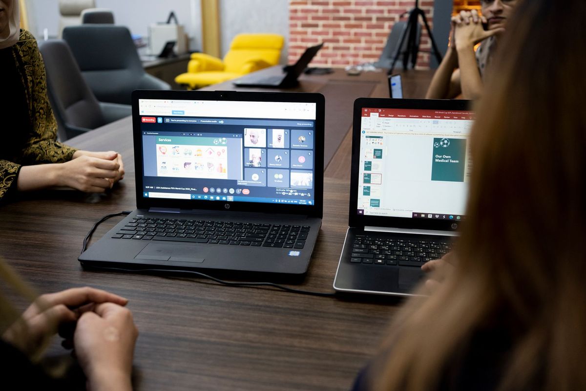 Two open laptops on a meeting table with people working around them