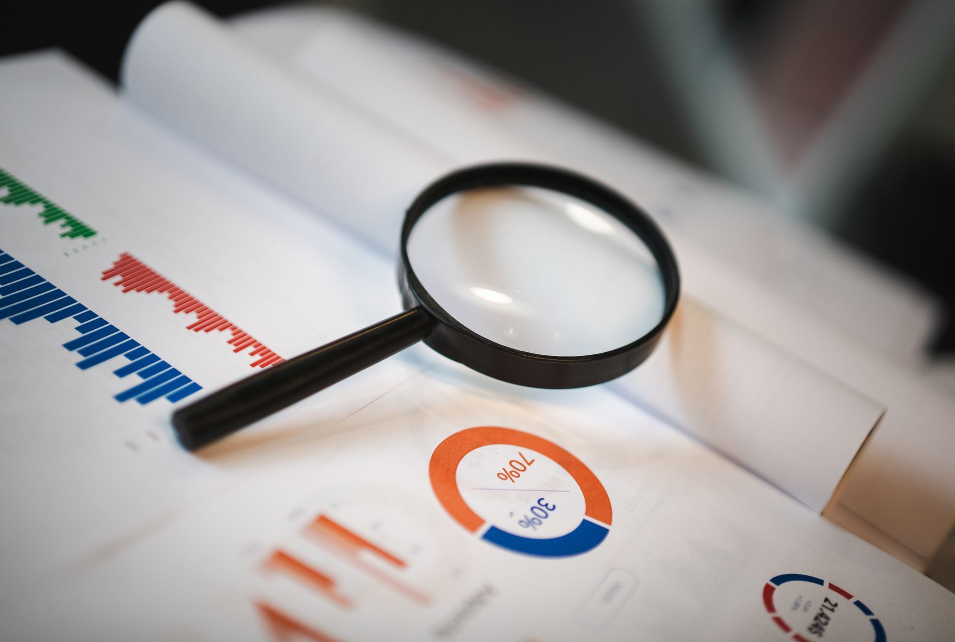 Magnifying glass resting on printed charts and graphs