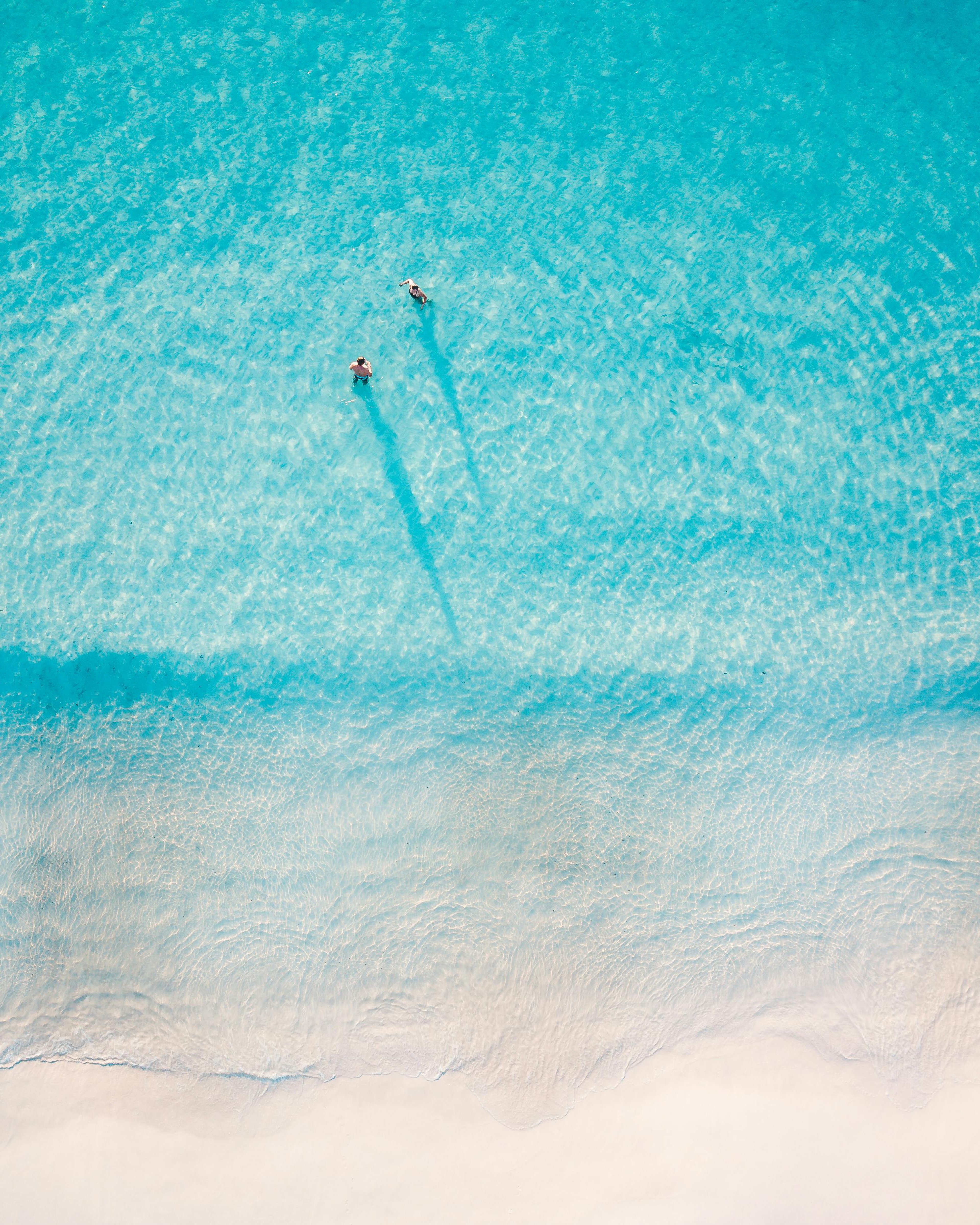 Two people swimming in clear turquoise water near a sandy shoreline