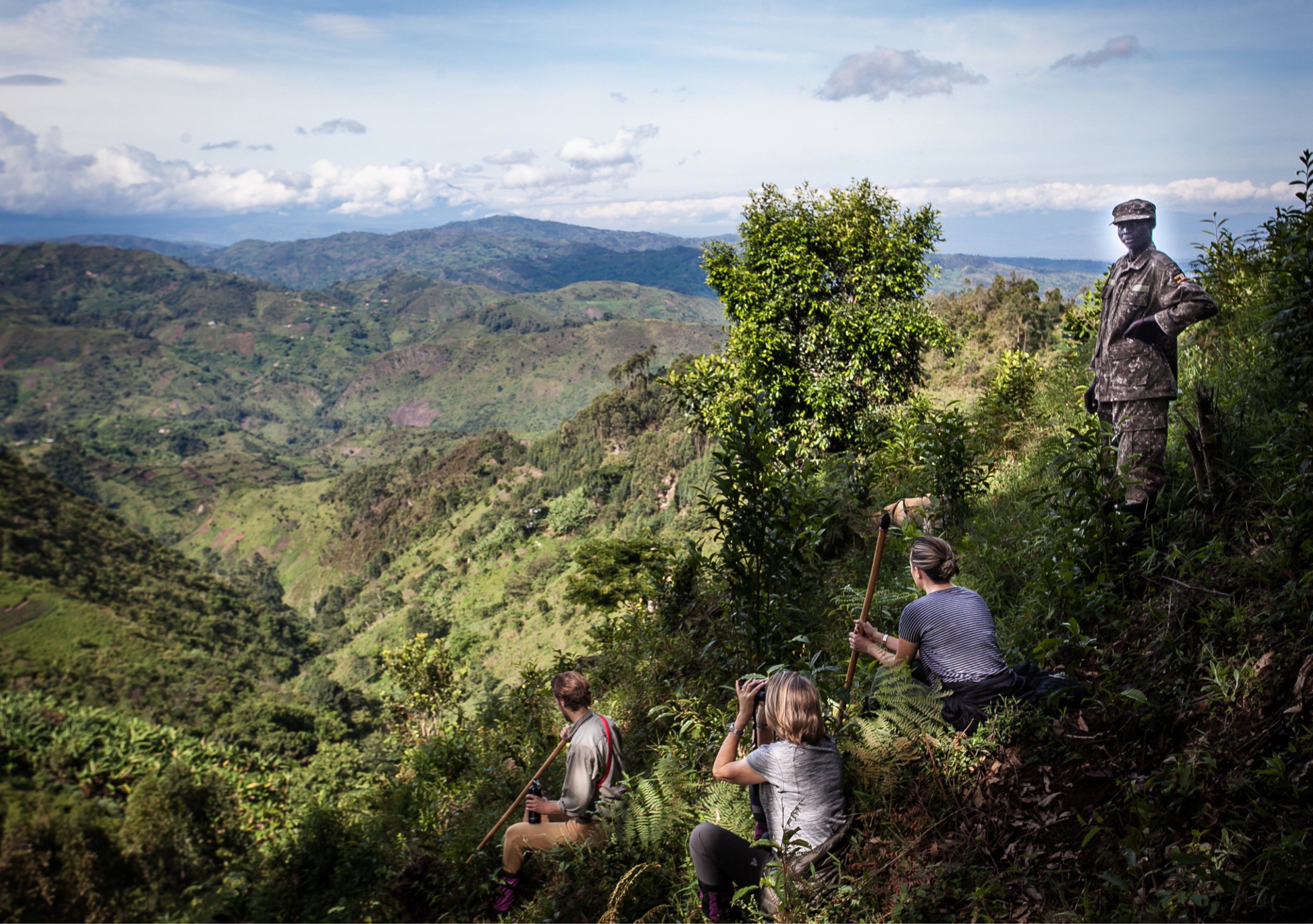 Tourists sitting on a hillside, accompanied by a guide, enjoying a view of the vast, green landscape below