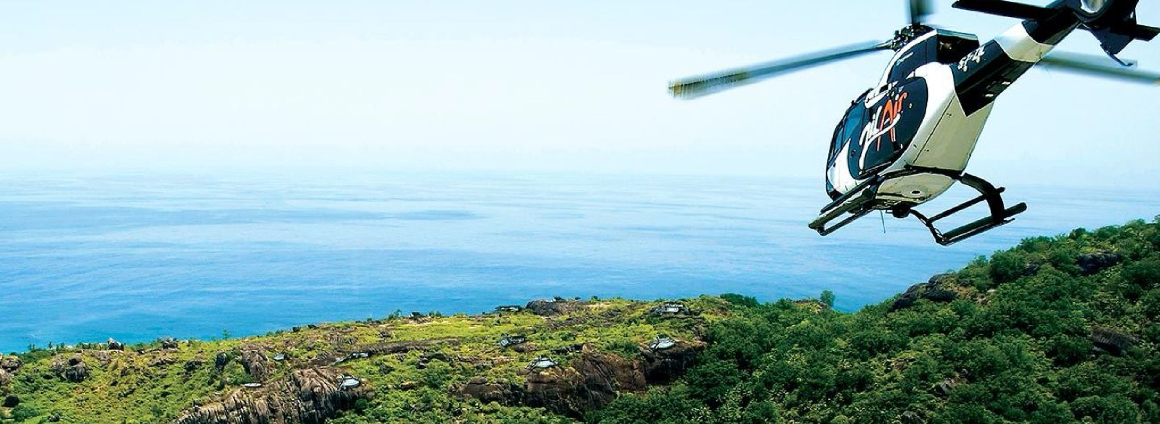 Helicopter flying over lush green hills by the ocean