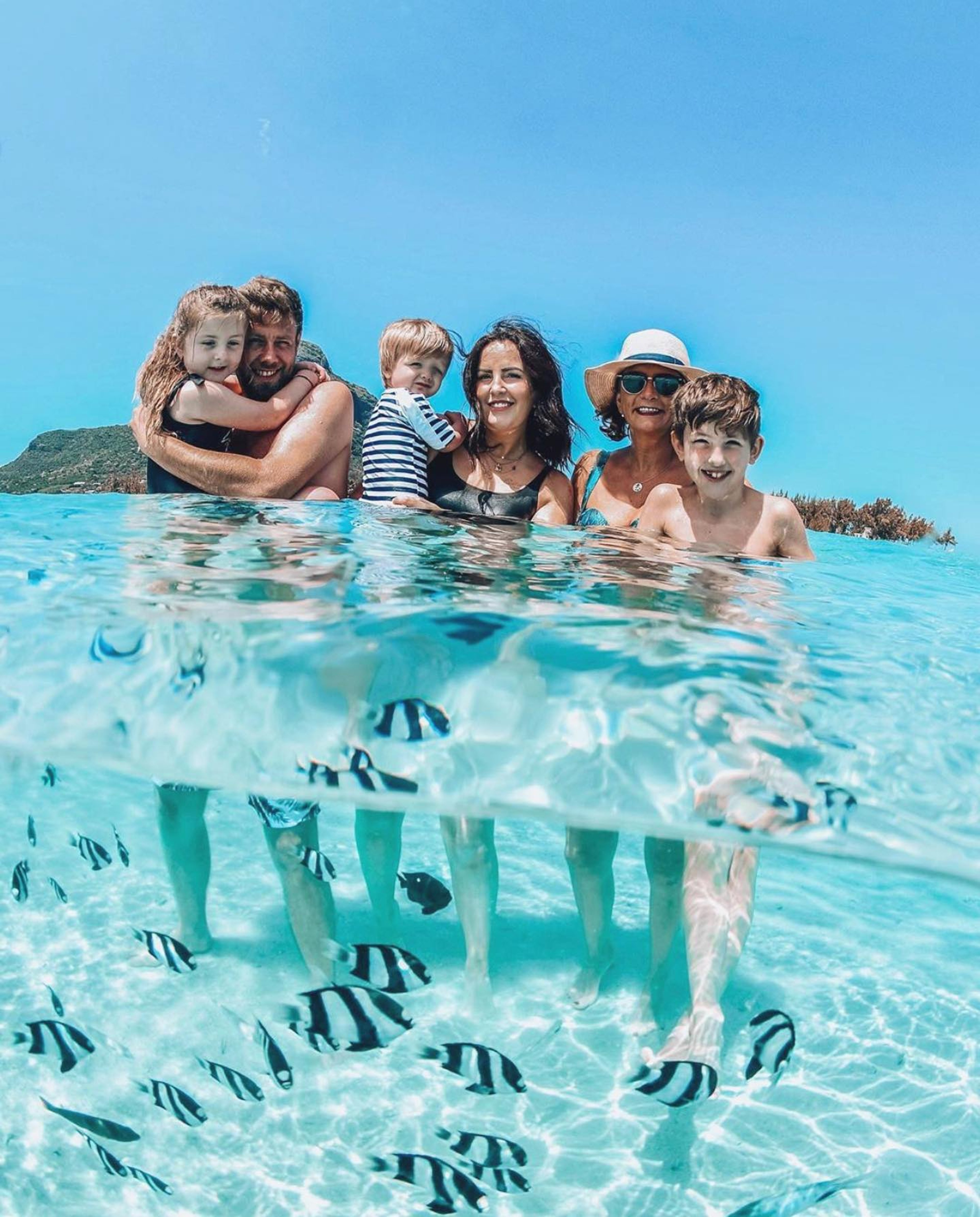 Family standing in shallow clear water with fish swimming below the surface