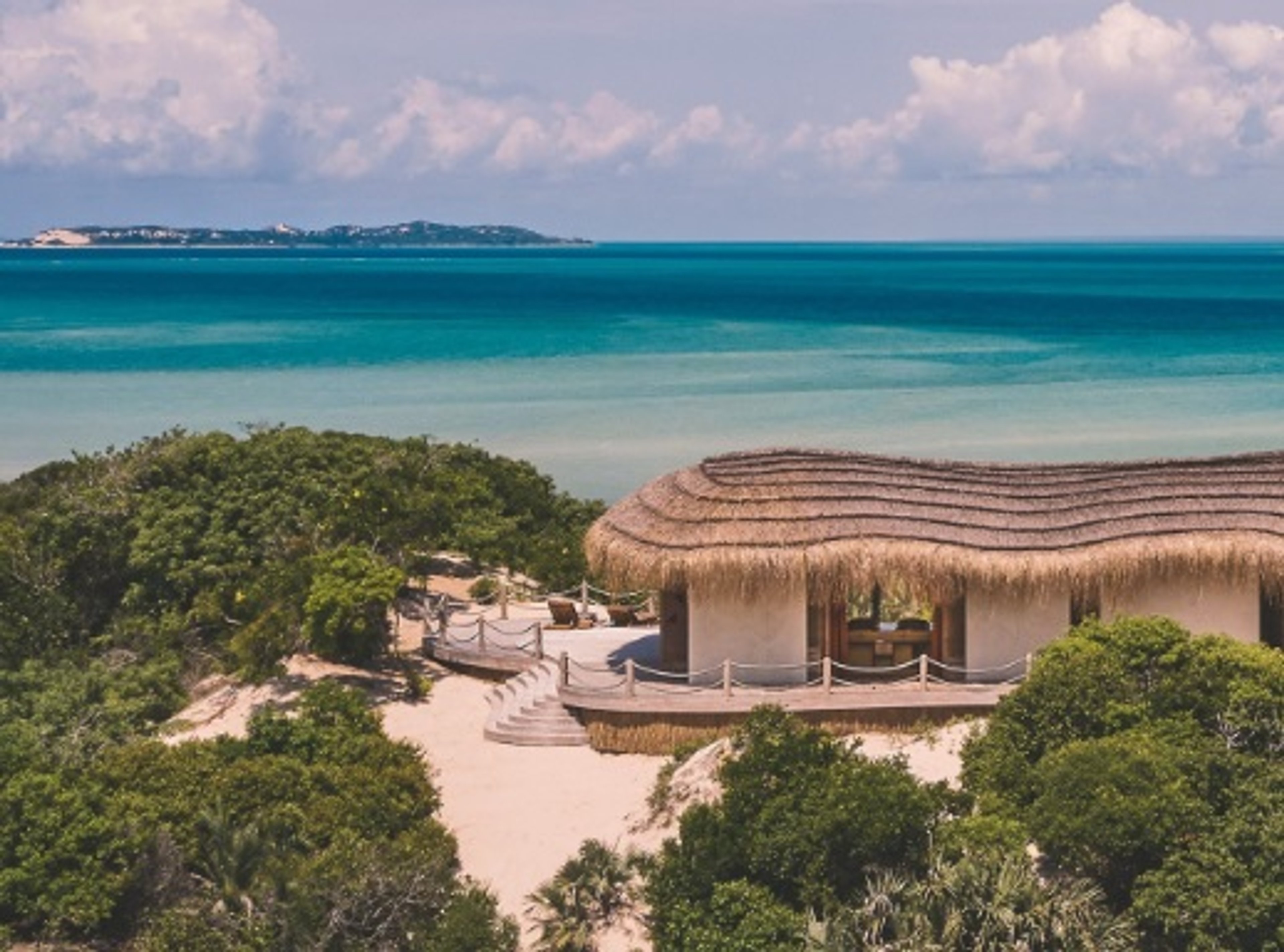 Beachfront villa with a thatched roof overlooking turquoise ocean waters