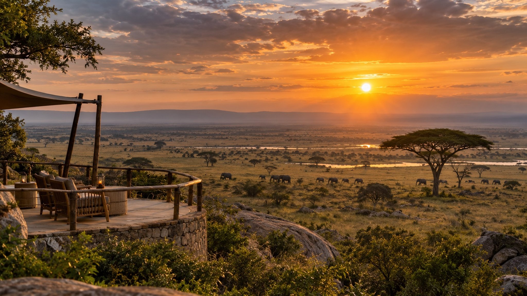 A tented deck above a classic savanna with elephants and acacia trees at sunset