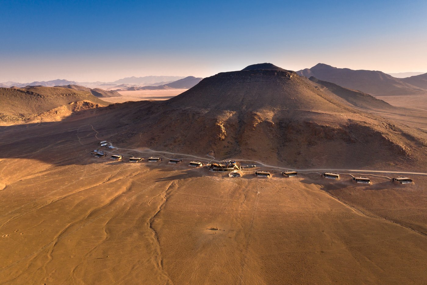 Aerial view of a desert lodge with cabins lined along the base of a hill