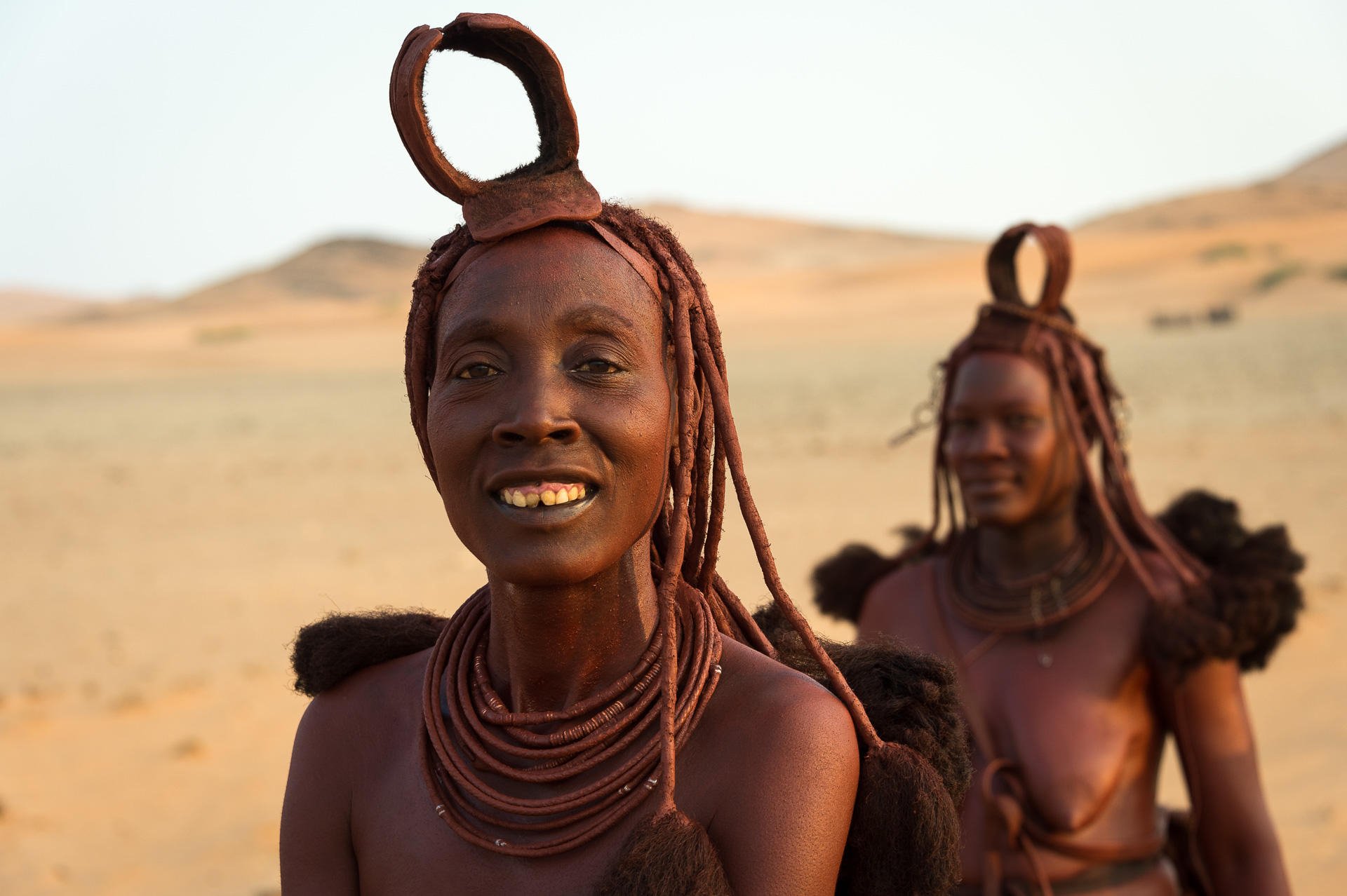 Two Himba women in traditional attire standing in a desert landscape