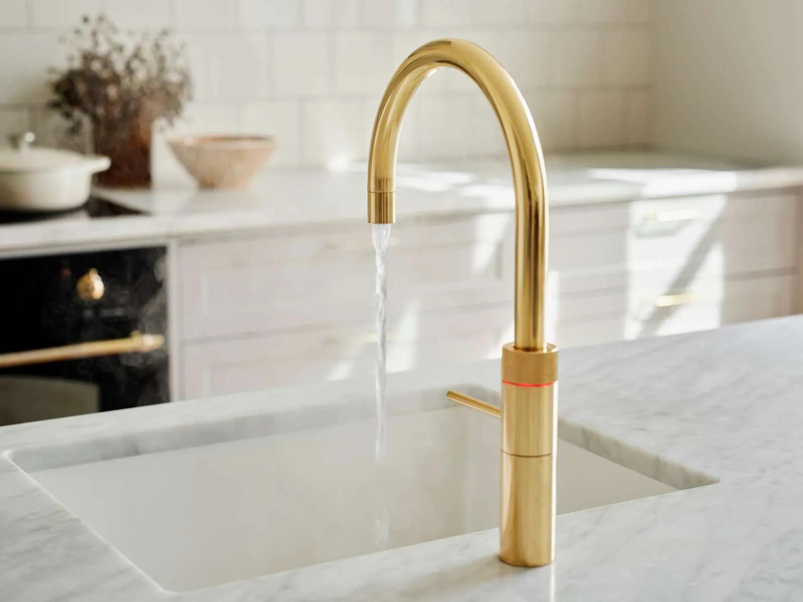 Quooker-kran i messing med kokende vann over en vask i marmor