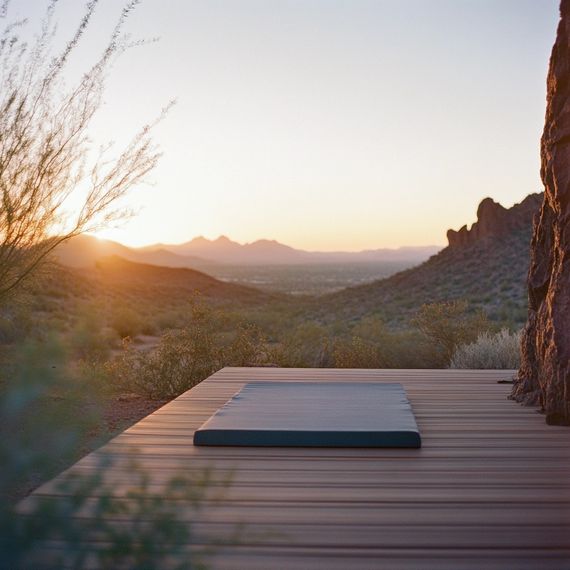 Bare cushion on a wooden deck overlooking a hazy desert valley at sunset