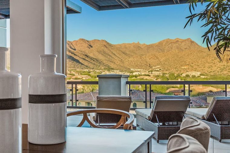 Covered terrace lounge chairs framing a view over tile rooftops to bare mountains