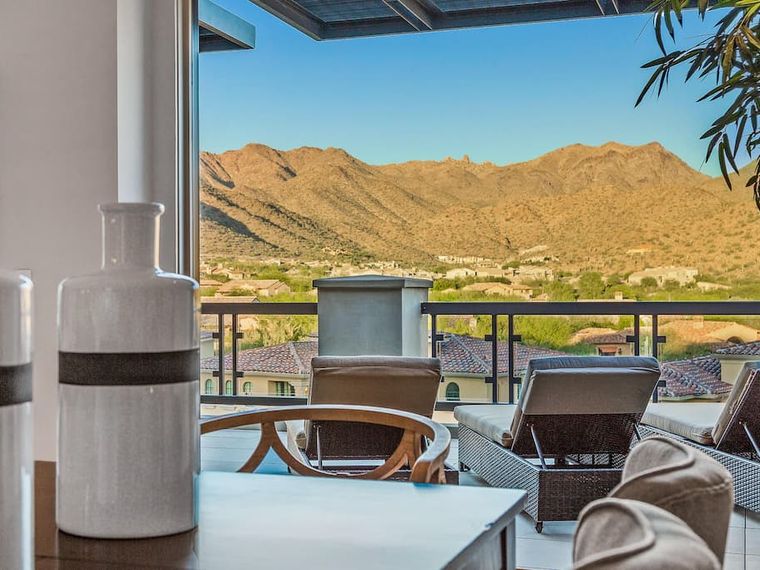 Covered terrace lounge chairs framing a view over tile rooftops to bare mountains