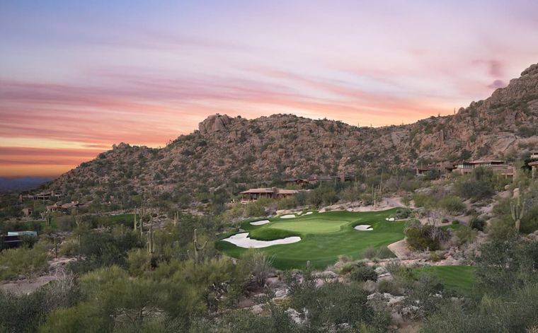 Golf green tucked below a granite boulder hillside dotted with low desert homes