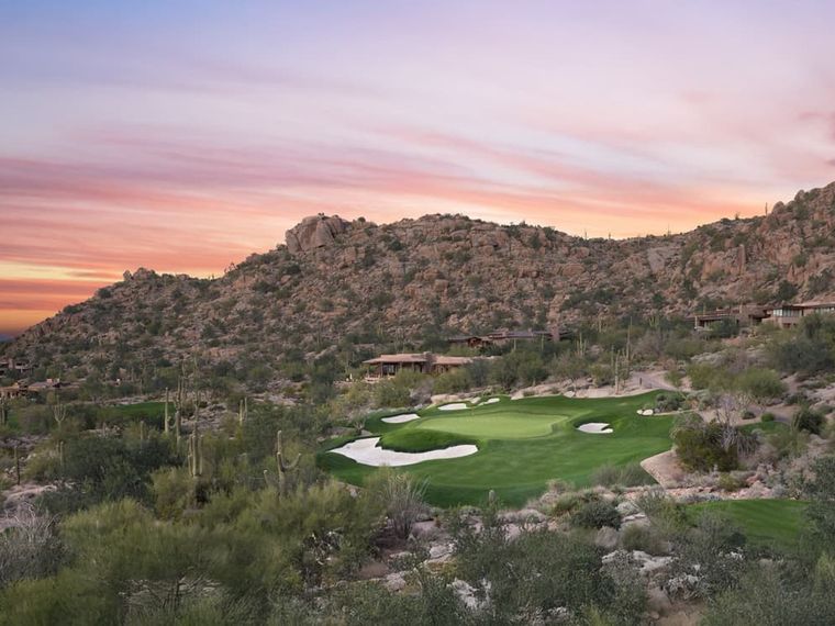 Golf green tucked below a granite boulder hillside dotted with low desert homes