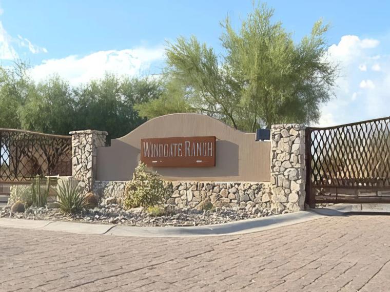 Stone and stucco entry monument lettered WINDGATE RANCH beside a paver drive and metal gate, desert planting around it