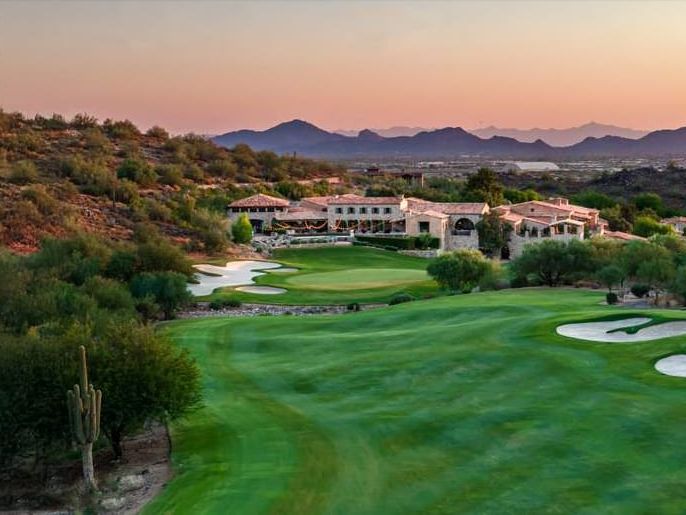 Broad fairway and bunkers curving below a hillside of tile-roofed homes, a mountain slope rising on the left