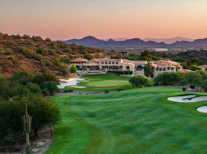 Broad fairway and bunkers curving below a hillside of tile-roofed homes, a mountain slope rising on the left