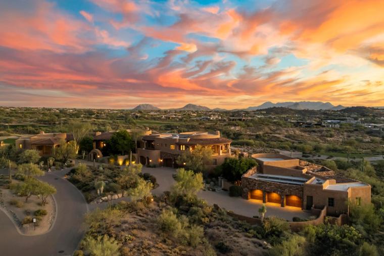 Aerial view of adobe-style hillside estates lit at sunset beneath streaked pink clouds