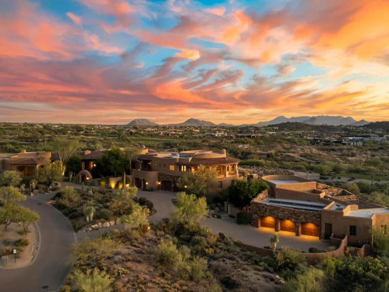 Aerial view of adobe-style hillside estates lit at sunset beneath streaked pink clouds
