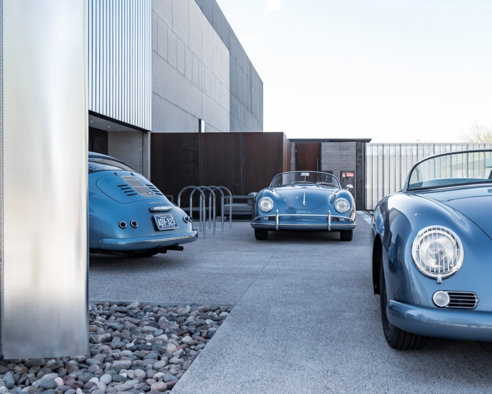 Vintage light-blue convertible sports cars parked in a row outside a modern garage building