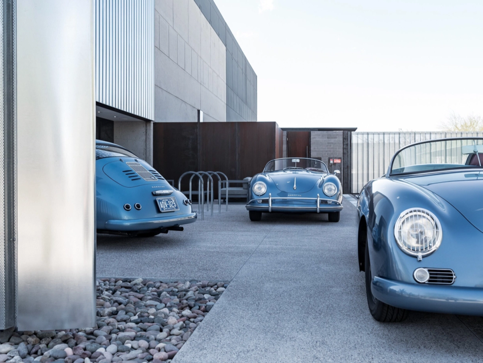 Vintage light-blue convertible sports cars parked in a row outside a modern garage building
